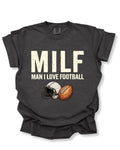 Flat lay of a pepper Comfort Colors t-shirt featuring the distressed ivory text "MILF" with the phrase "MAN I LOVE FOOTBALL" underneath, along with a vintage-style white football helmet and brown football graphic. The shirt is displayed on a white background with rolled sleeves, creating a bold and humorous football fan design perfect for football moms, tailgates, and game day.