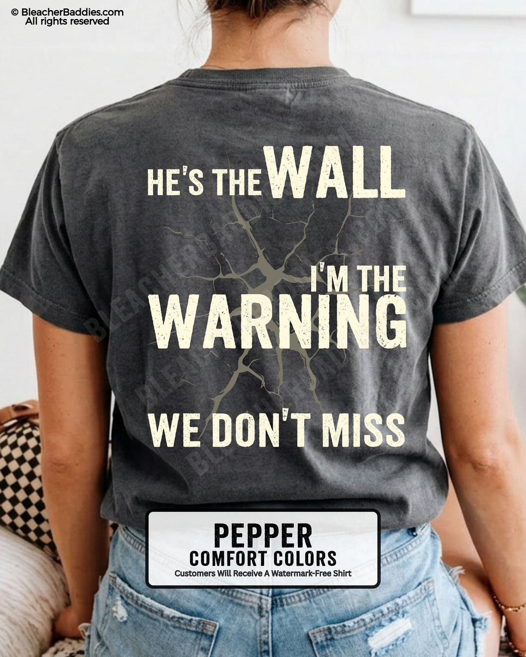 Woman wearing a pepper football mom game day shirt shown from the back featuring a large distressed cream graphic that reads “He’s the Wall I’m the Warning We Don’t Miss.”