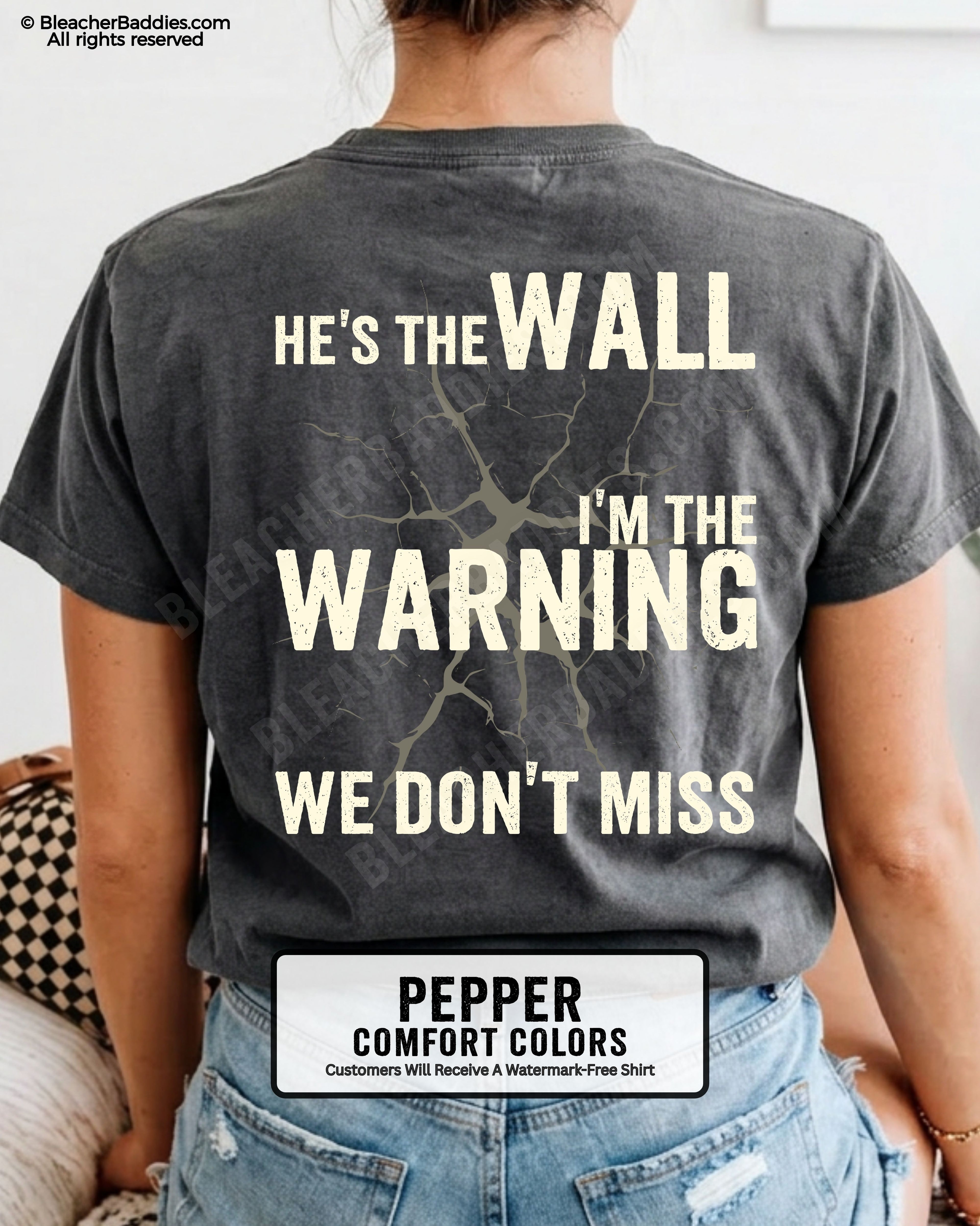 Woman wearing a pepper football mom game day shirt shown from the back featuring a large distressed cream graphic that reads “He’s the Wall I’m the Warning We Don’t Miss.”
