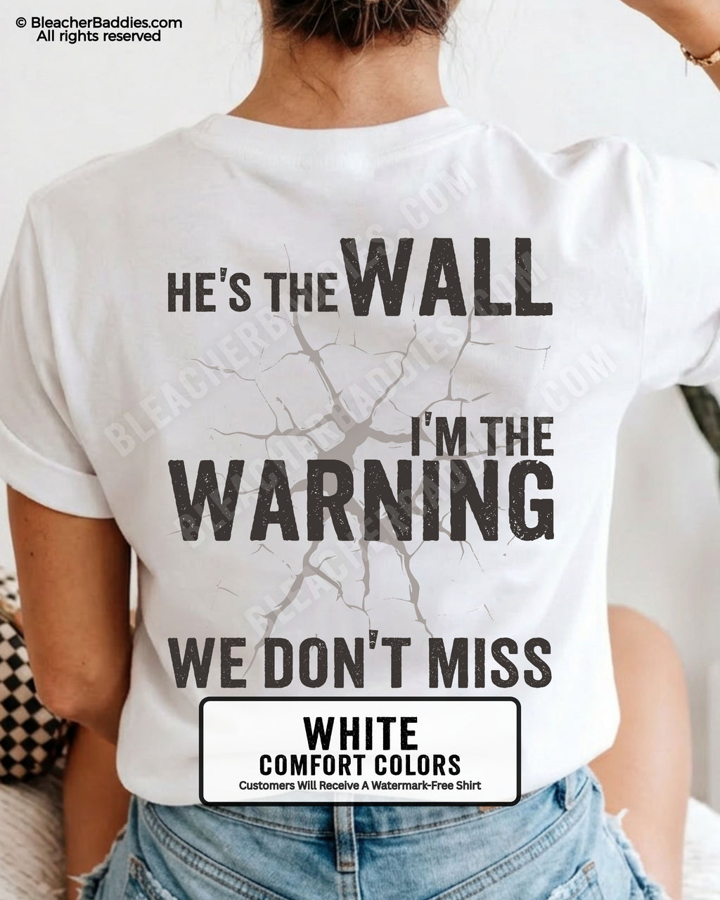 Woman wearing a white football mom game day shirt shown from the back featuring a large distressed black graphic that reads “He’s the Wall I’m the Warning We Don’t Miss.”