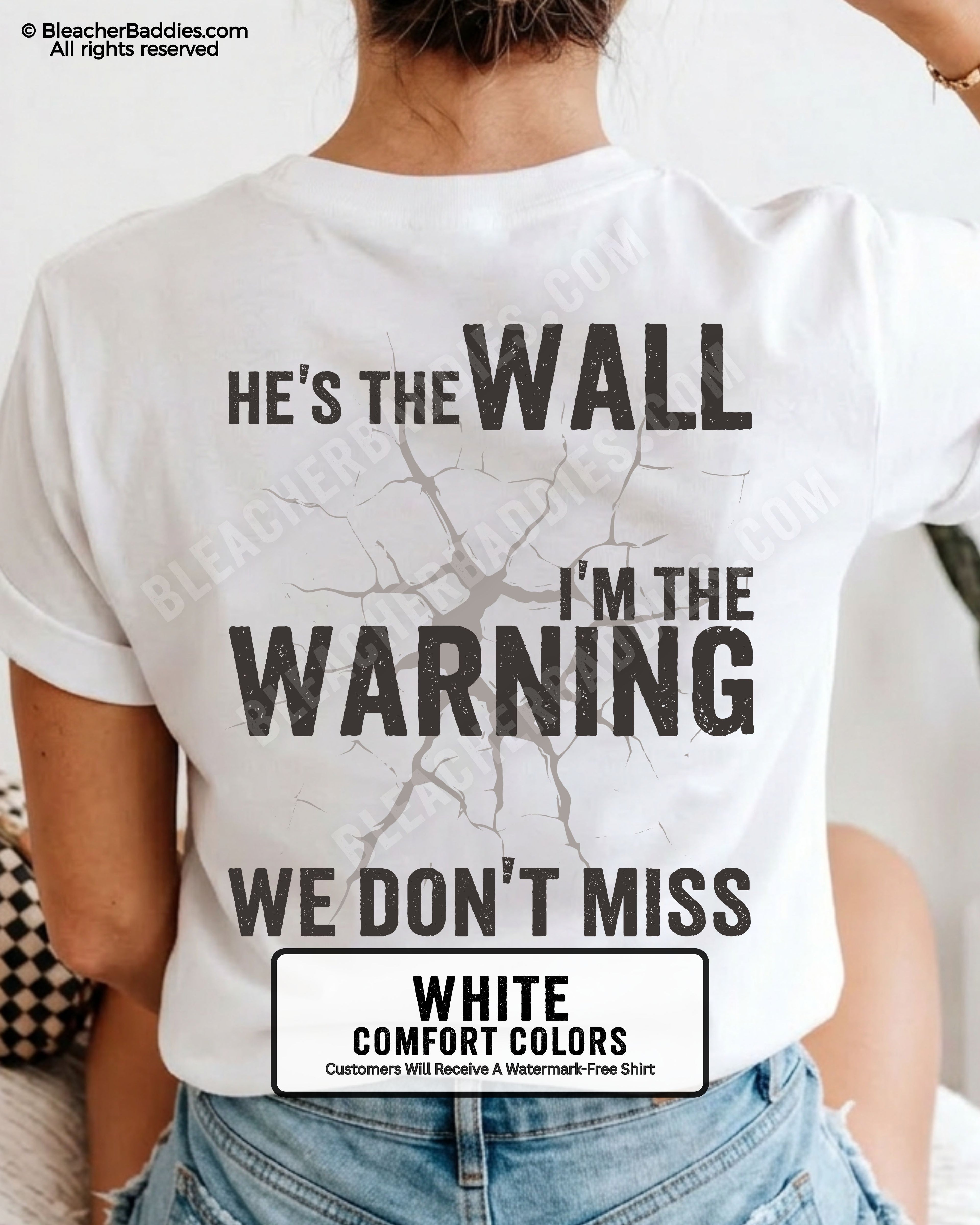 Woman wearing a white football mom game day shirt shown from the back featuring a large distressed black graphic that reads “He’s the Wall I’m the Warning We Don’t Miss.”