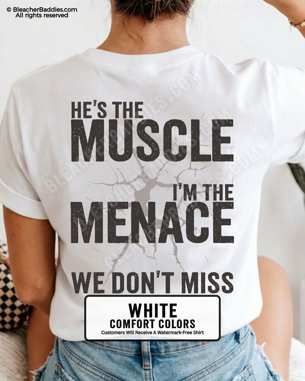 Woman wearing WHITE Comfort Colors football mom game day shirt with back design that reads “He’s the muscle I’m the menace we don’t miss” in distressed black text with cracked graphic and chambray color label shown
