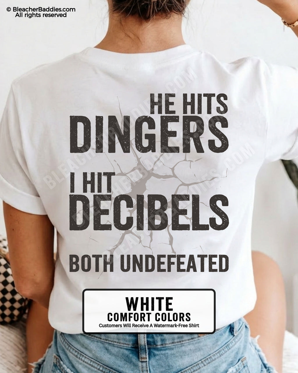 White Comfort Colors baseball mom graphic tee with oversized distressed lettering reading “He Hits Dingers I Hit Decibels Both Undefeated” across the back