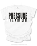 White graphic t-shirt with bold distressed “PRESSURE IS A PRIVILEGE” text centered on the front of a relaxed fit short sleeve shirt displayed on a neutral background.