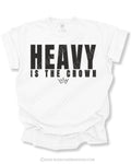 White graphic t-shirt featuring bold black “HEAVY IS THE CROWN” text with a minimalist crown graphic underneath displayed on a relaxed fit short sleeve shirt against a white background.