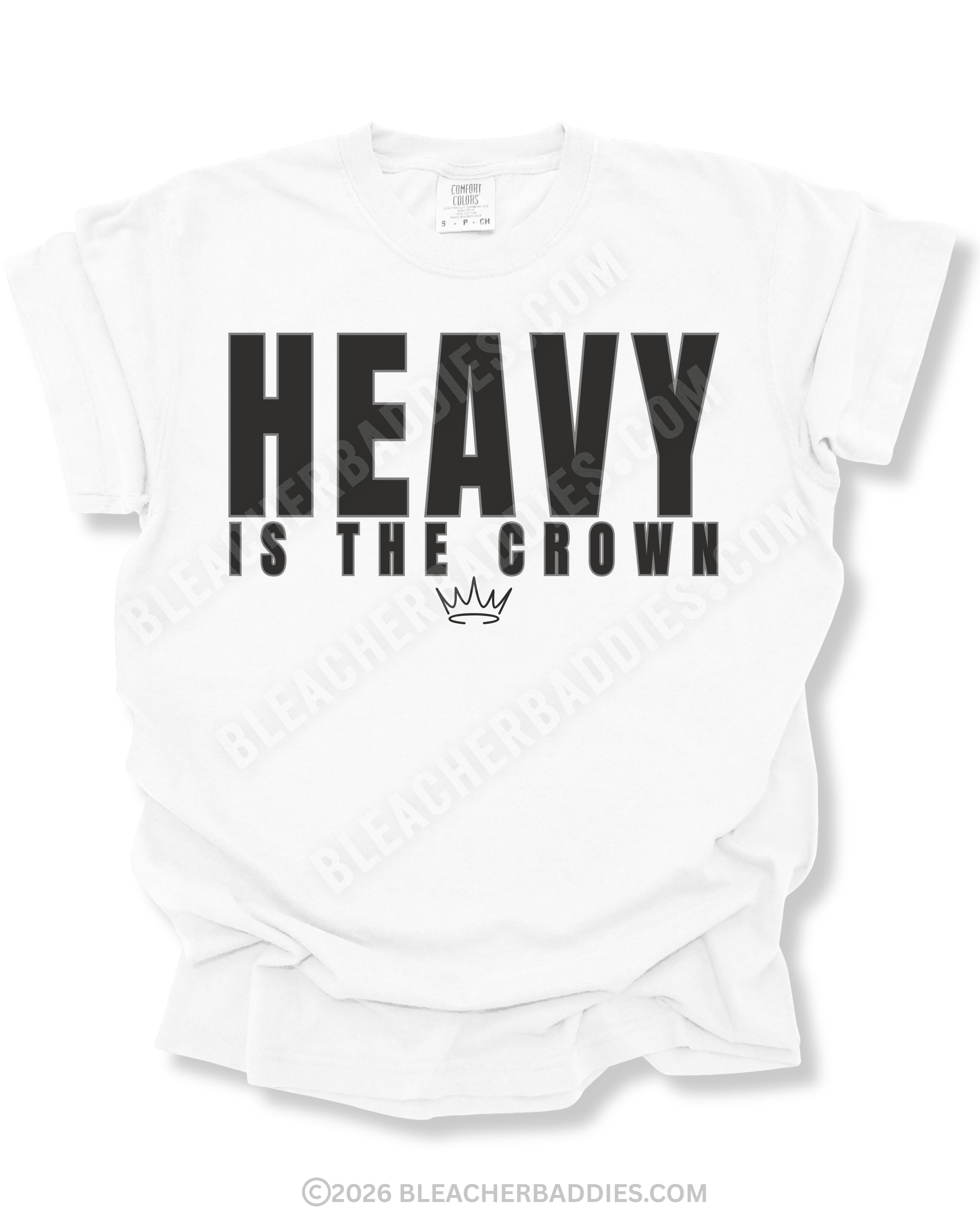 White graphic t-shirt featuring bold black “HEAVY IS THE CROWN” text with a minimalist crown graphic underneath displayed on a relaxed fit short sleeve shirt against a white background.