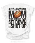 White Comfort Colors t-shirt with bold black back graphic reading “Just a Football Mom Who Doesn’t Ever Sit Down or Shut Up” with a football illustration centered in the design