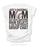 White baseball mom game day shirt with distressed black text reading “Just a baseball mom out here surviving rain delays and the team parents group chat” with baseball graphic replacing the O in MOM