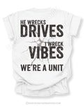 White t-shirt shown from the back featuring a large distressed black graphic that reads “He Wrecks Drives I Wreck Vibes We’re a Unit” with a cracked texture effect.