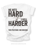 Flat lay of a white Comfort Colors t-shirt featuring the phrase "He Hits Hard I Yell Harder" with a distressed football graphic and "Two Positions One Mission" printed on the back.