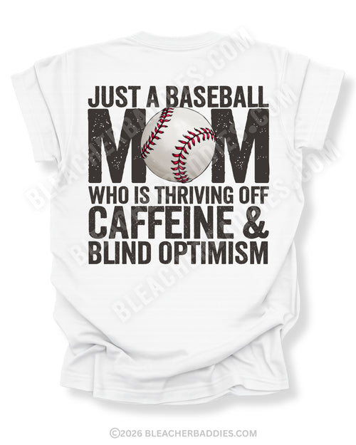 White baseball mom graphic tee featuring distressed black text reading “Just a baseball mom who is thriving off caffeine and blind optimism” with baseball graphic centered in the word MOM