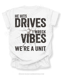 White Comfort Colors baseball mom shirt with distressed oversized back graphic reading “He Hits Drives I Wreck Vibes We’re A Unit” in bold black typography with cracked background effect and BleacherBaddies.com watermark across design.