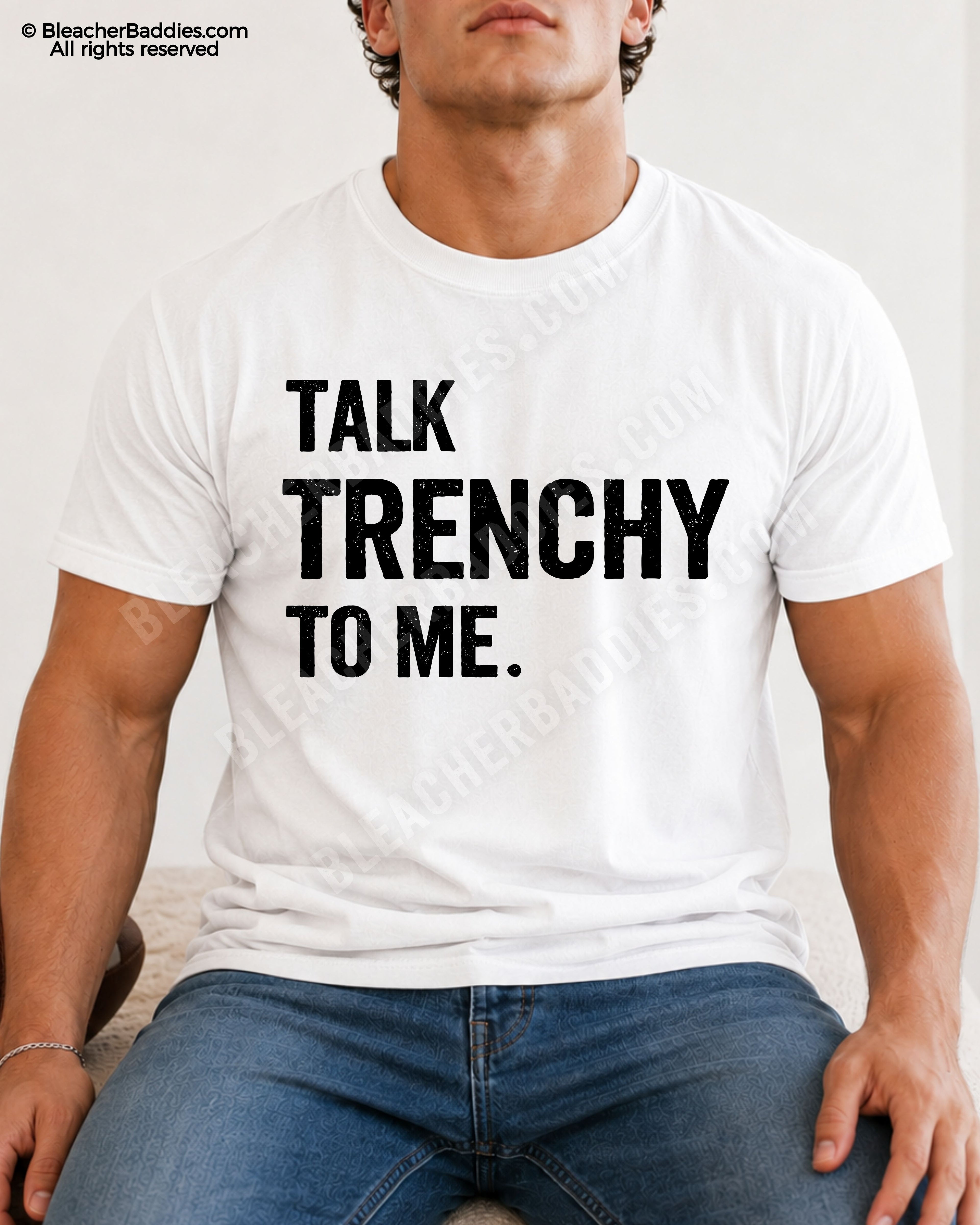 Athletic male model sitting while wearing a white Comfort Colors 1717 t-shirt with "Talk Trenchy to Me" football lineman graphic and distressed blue jeans.