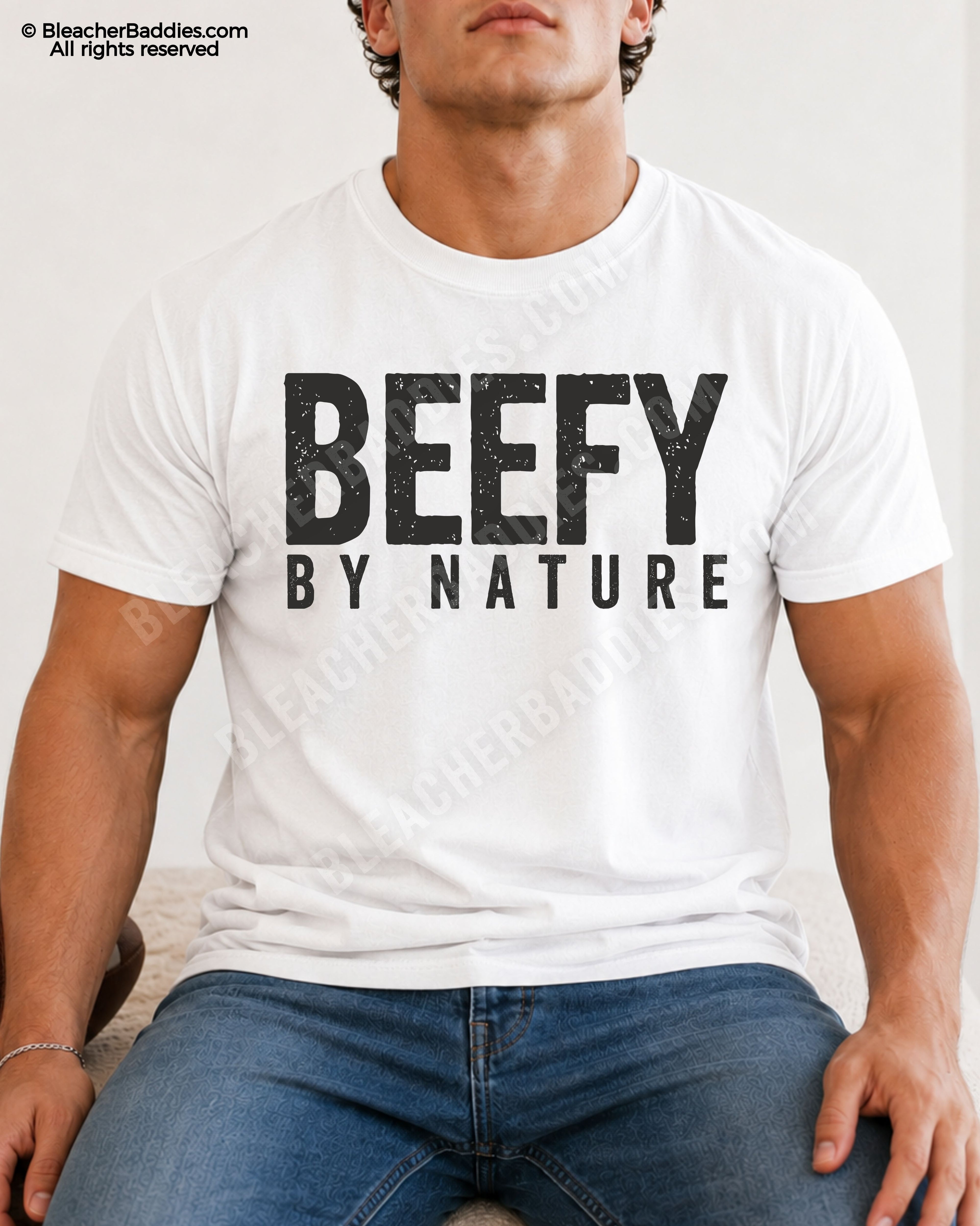 Male football player model wearing a white Comfort Colors “Beefy By Nature” football shirt with distressed black typography while seated indoors in jeans.
