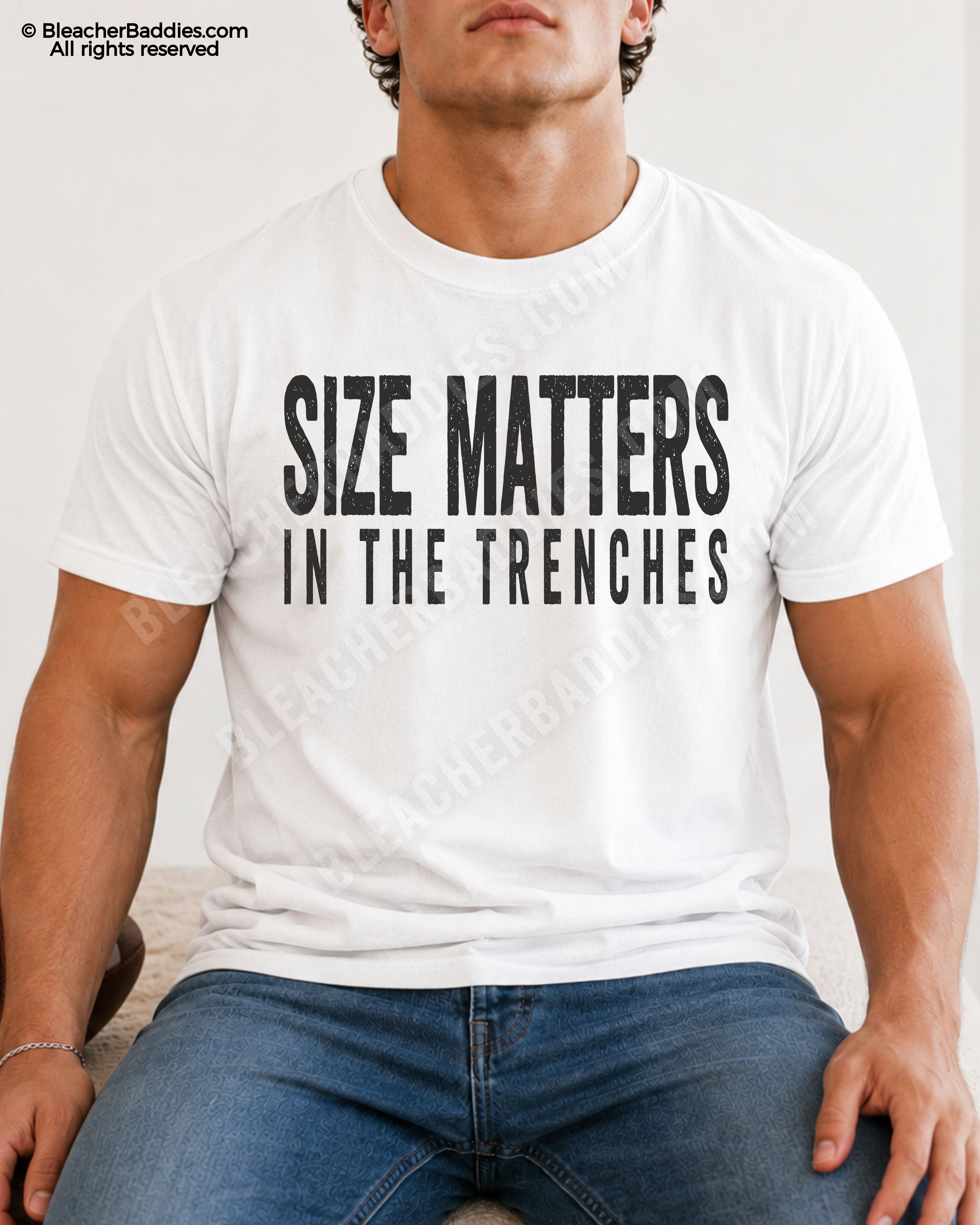Male football player model sitting indoors wearing a white Comfort Colors lineman shirt with distressed “Size Matters In The Trenches” graphic paired with jeans.