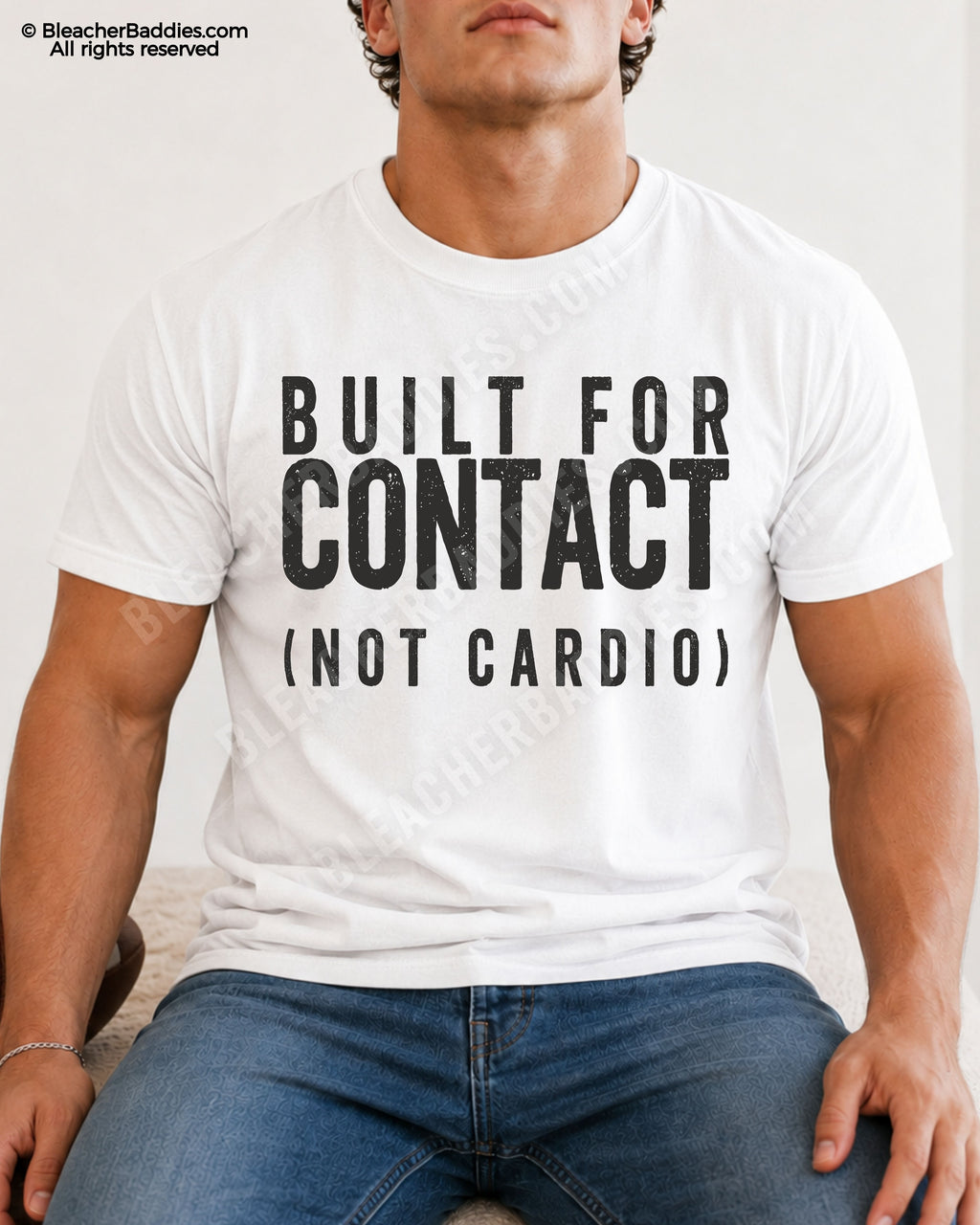 Male football player model wearing a white Comfort Colors “Built For Contact (Not Cardio)” football shirt with bold distressed typography while seated indoors in casual denim jeans.
