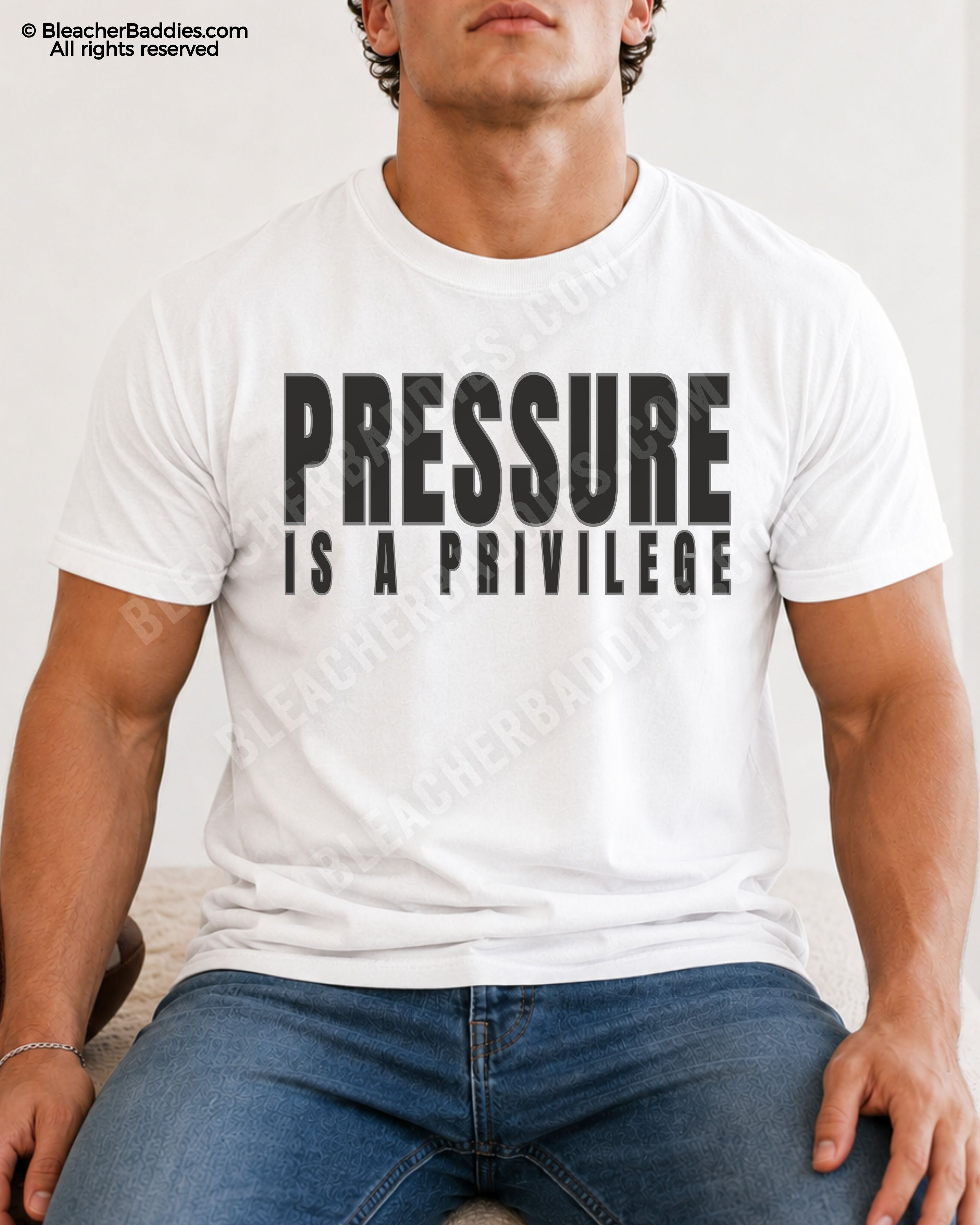 Young male athlete wearing a white motivational football graphic t-shirt with bold black “PRESSURE IS A PRIVILEGE” lettering while sitting indoors in jeans.