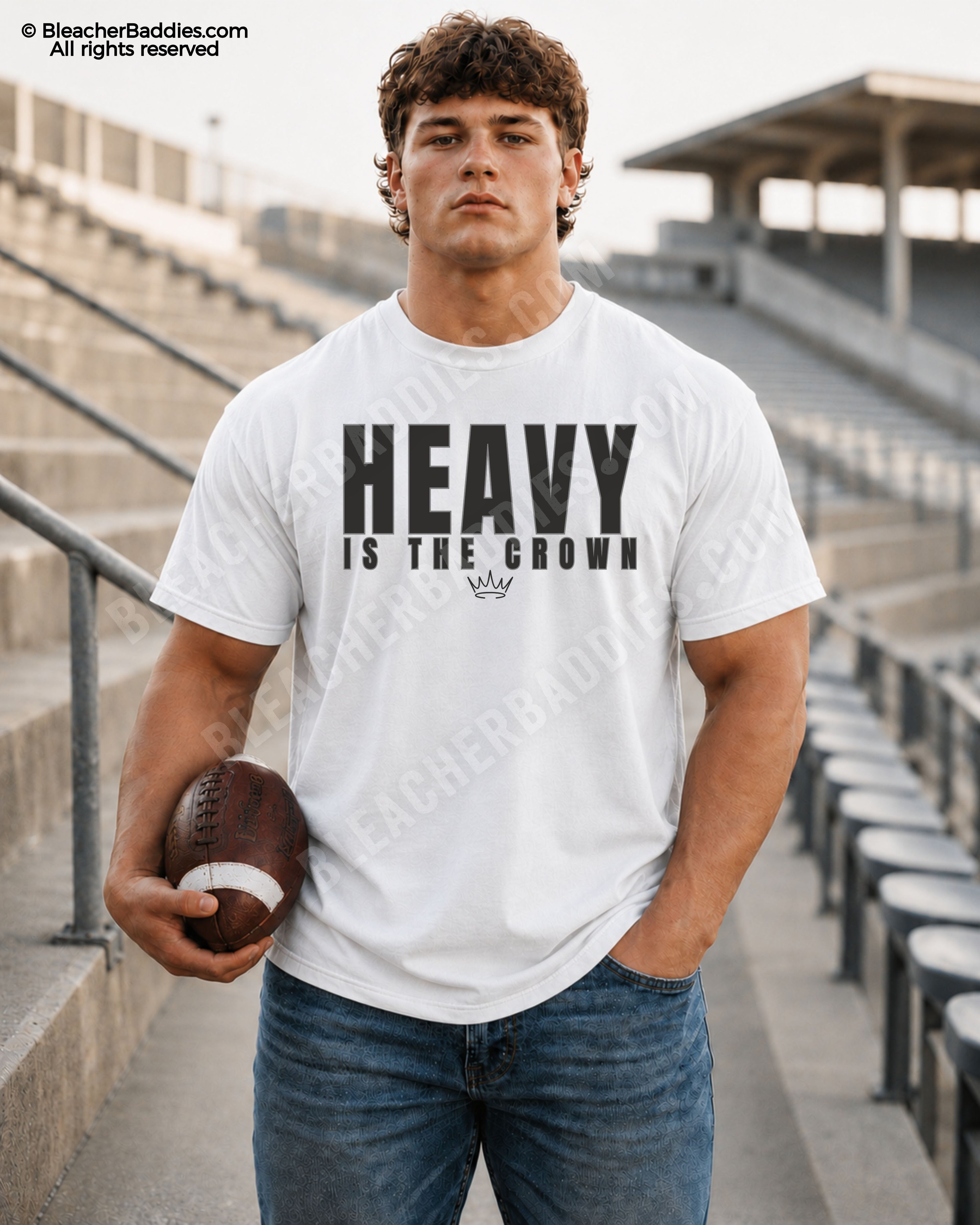 Football player standing in stadium bleachers wearing a white “HEAVY IS THE CROWN” athlete mindset graphic t-shirt while holding a football and wearing blue jeans.